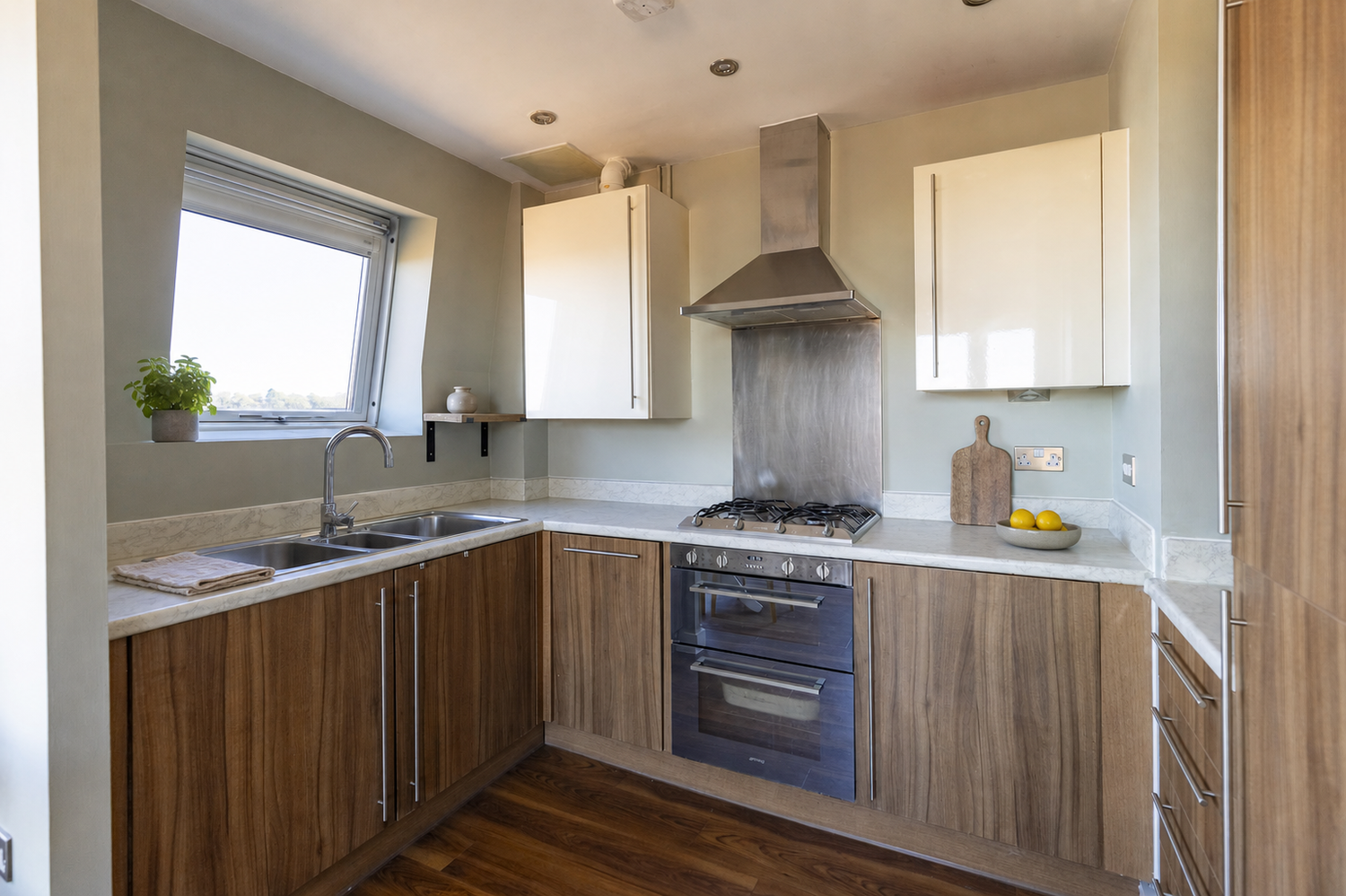 Modern kitchen with wood-effect cabinets, stainless steel range hood, gas hob, and white quartz countertops with natural light.