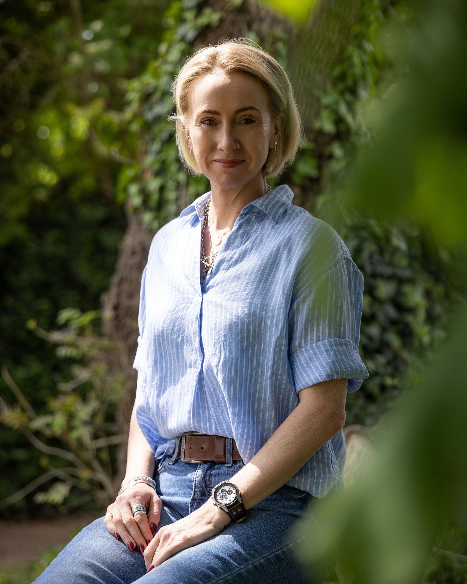 Personal branding portrait of a woman sitting outdoors surrounded by lush greenery in natural light.