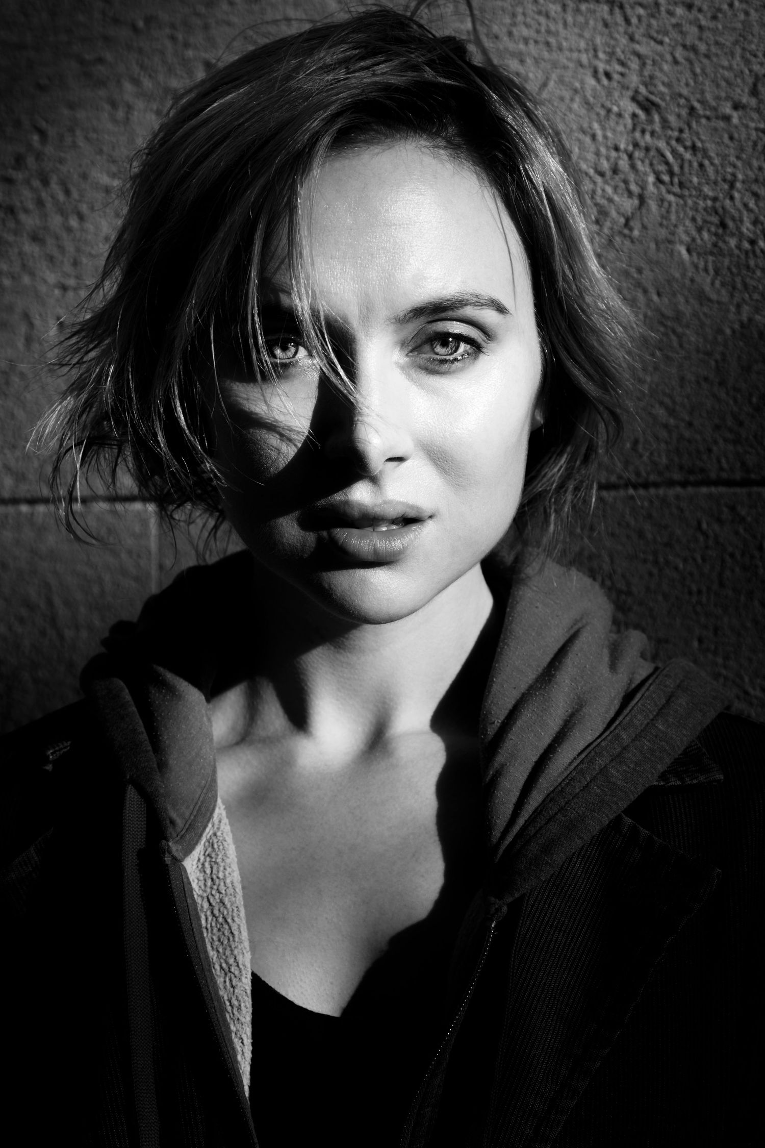 Black and white portrait of young woman with short hair, photographed with dramatic lighting against a textured studio backdrop.