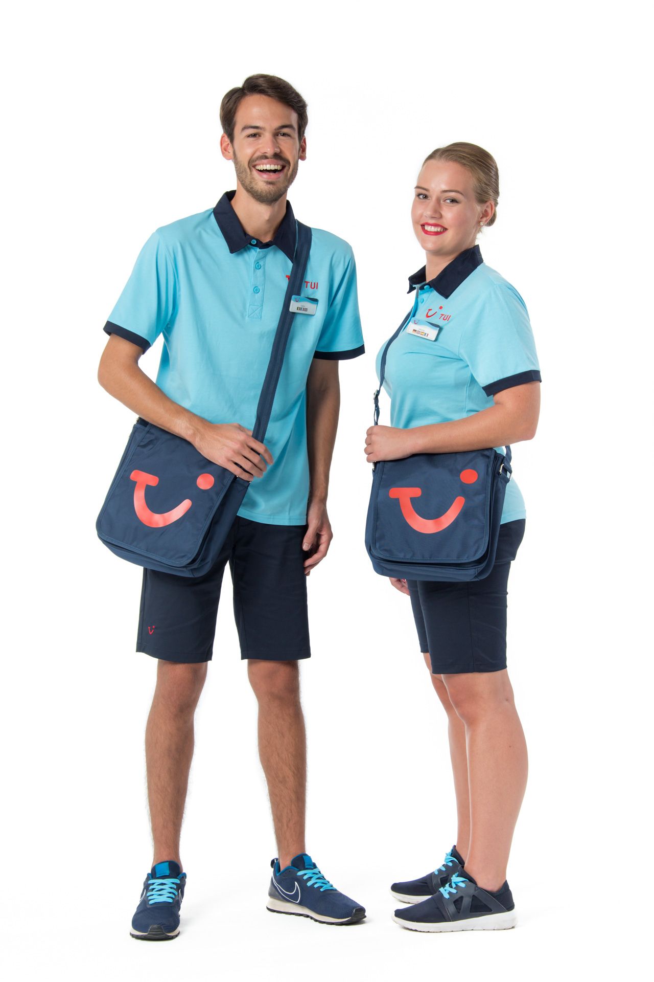 Two TUI workers in matching light blue uniforms and navy messenger bags with TUI smile logo stand together against white background.