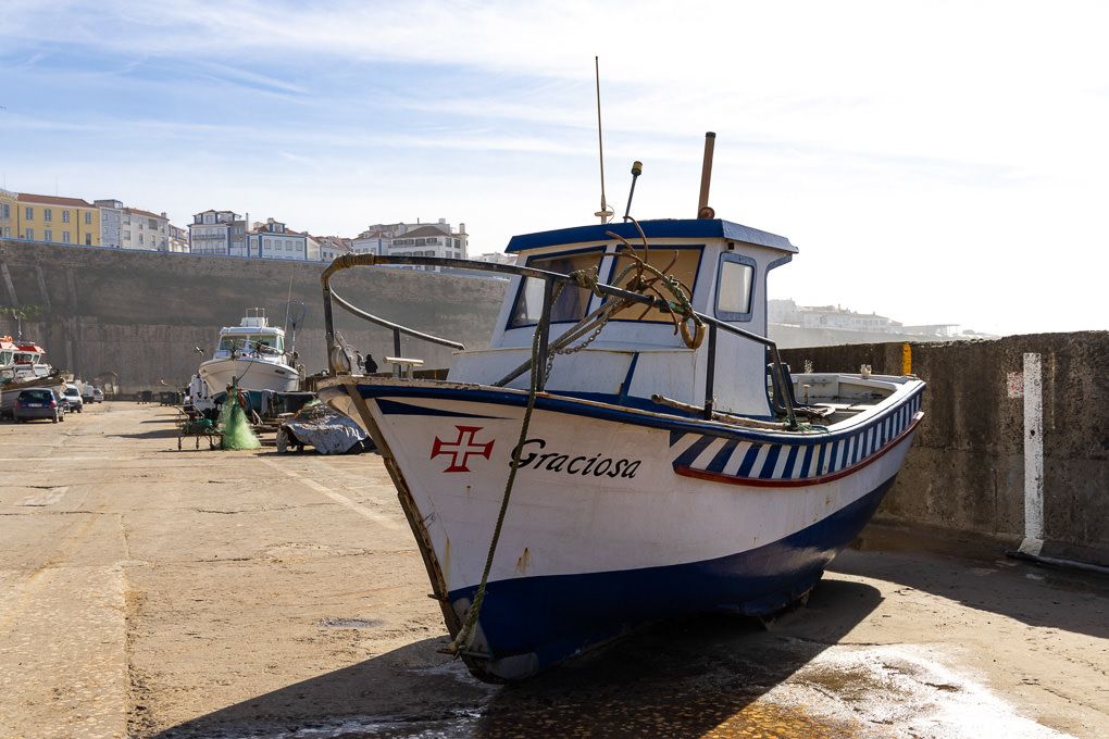 A blue and white fishing boat named The Beacon sits on dry land at harbor during low tide.