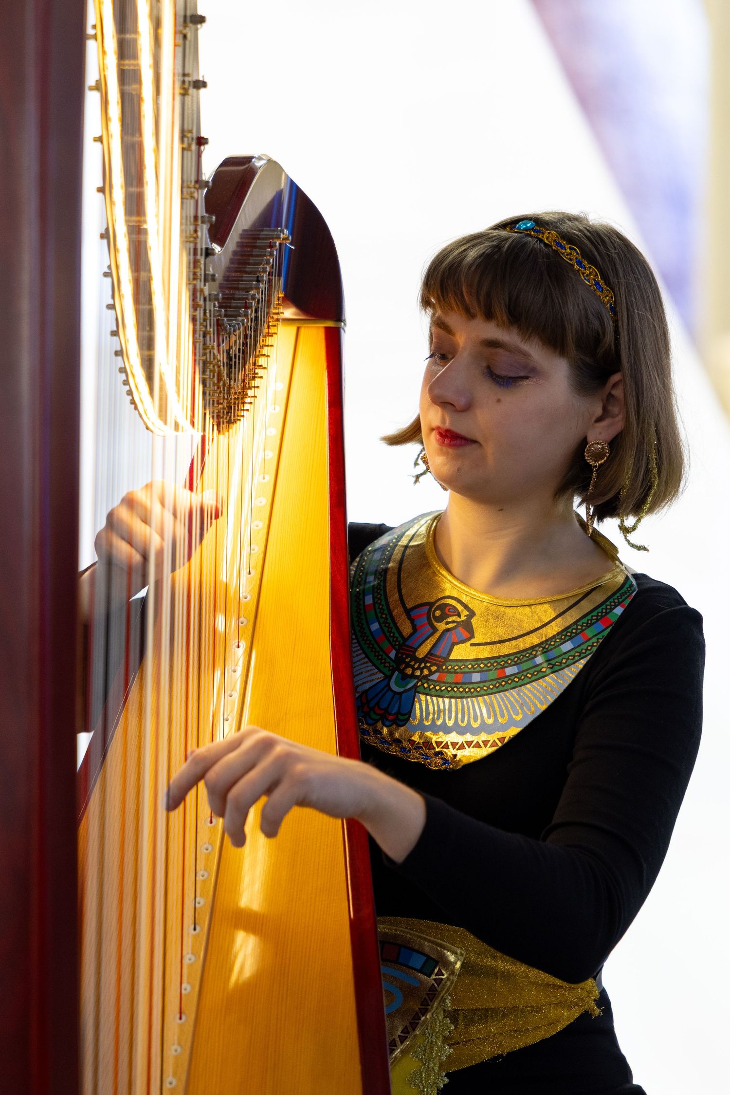 Young woman playing a golden harp wearing an Egyptian-inspired costume.