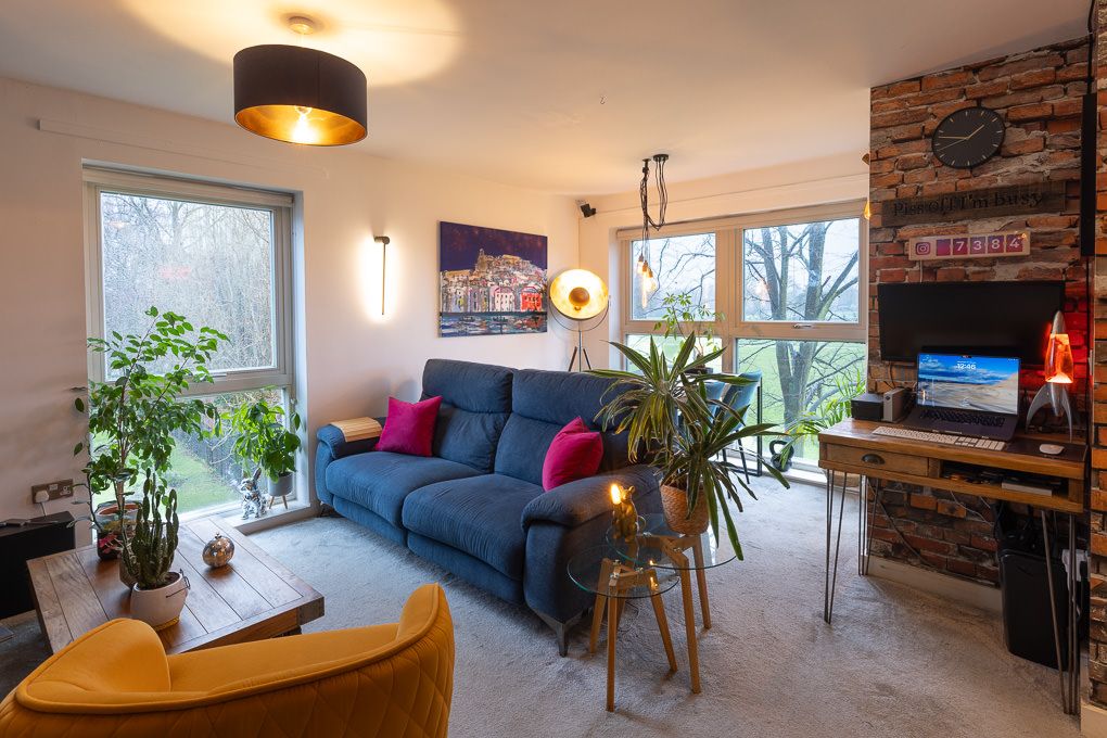 Interior photography of a modern living room with a blue sofa, a yellow chair, houseplants and large windows overlooking natural scenery.