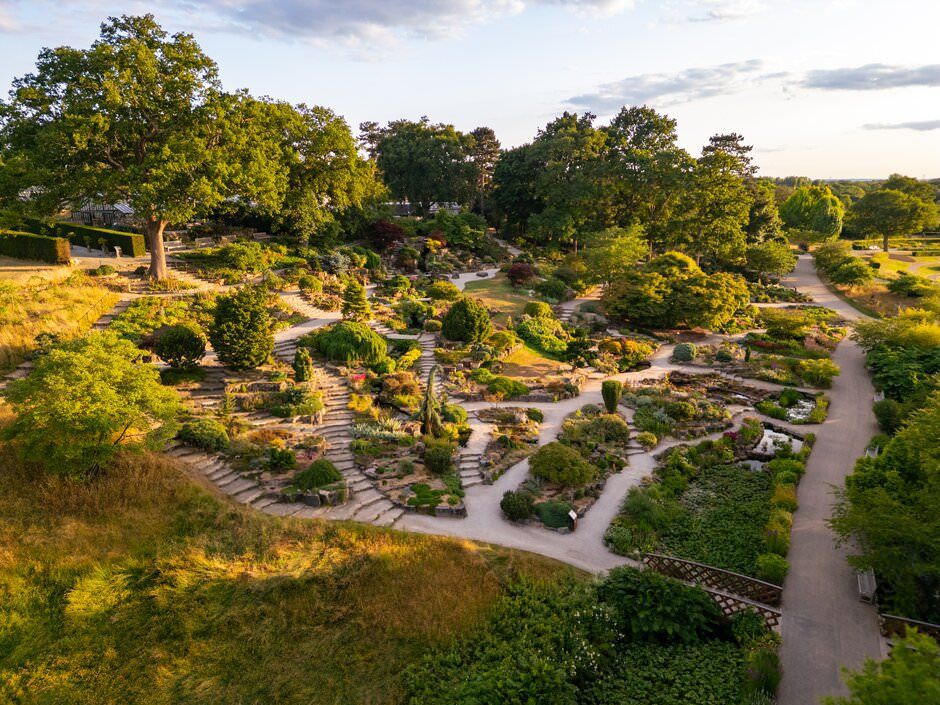 An elevated view of a winding garden path through landscaped rock gardens with trees at sunset.