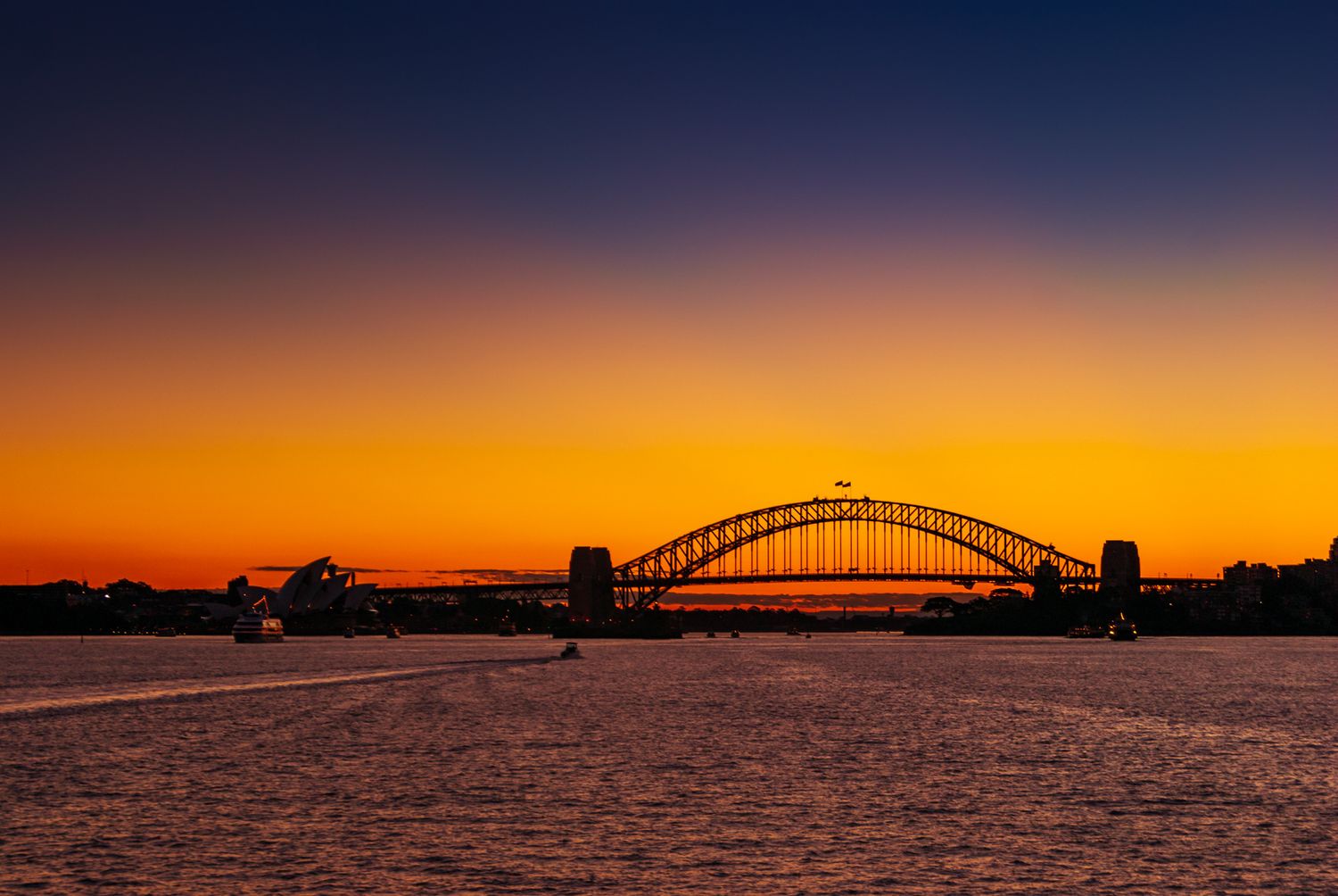 Iconic Sydney Harbour Bridge silhouetted against a vibrant orange and purple sunset sky over calm waters.