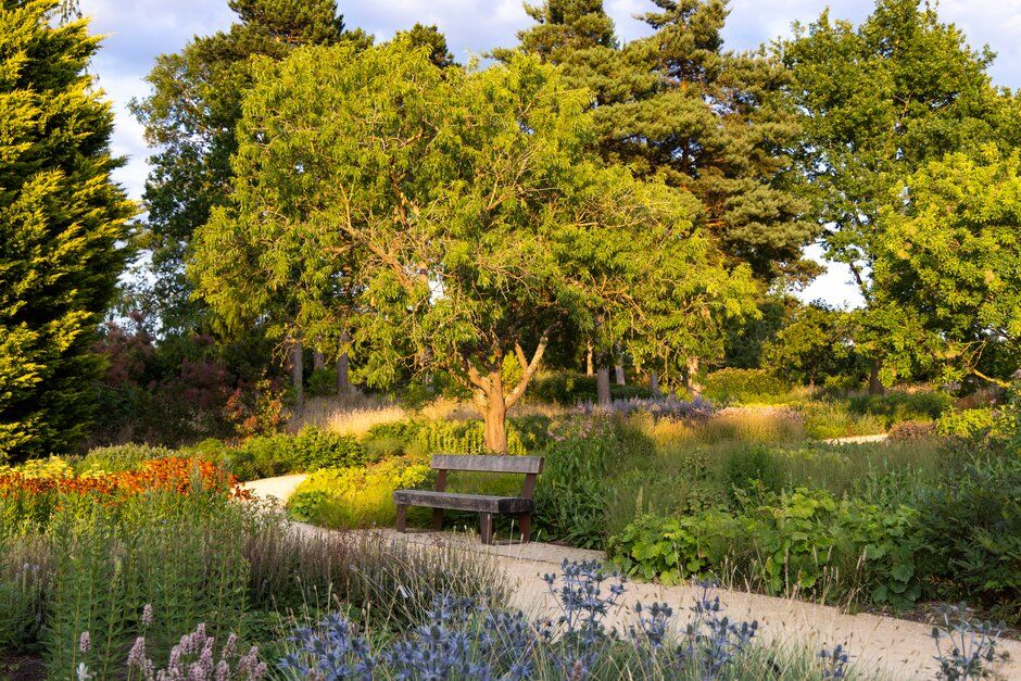Lush garden landscape features native plants and flowers surrounding a modern greenhouse facility.