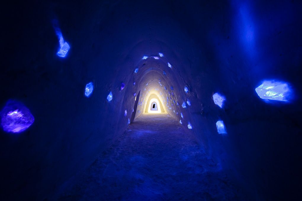 Illuminated ice cave interior glows with ethereal blue light and features a triangular opening in the distance. Ice Village Lapland.