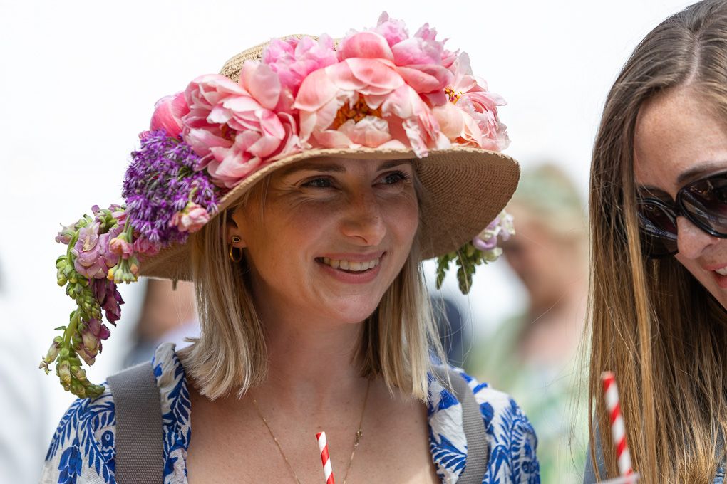 Press photography of a woman in a blue-and-white floral dress and sunglasses, relaxing on the grass during an outdoor gathering.