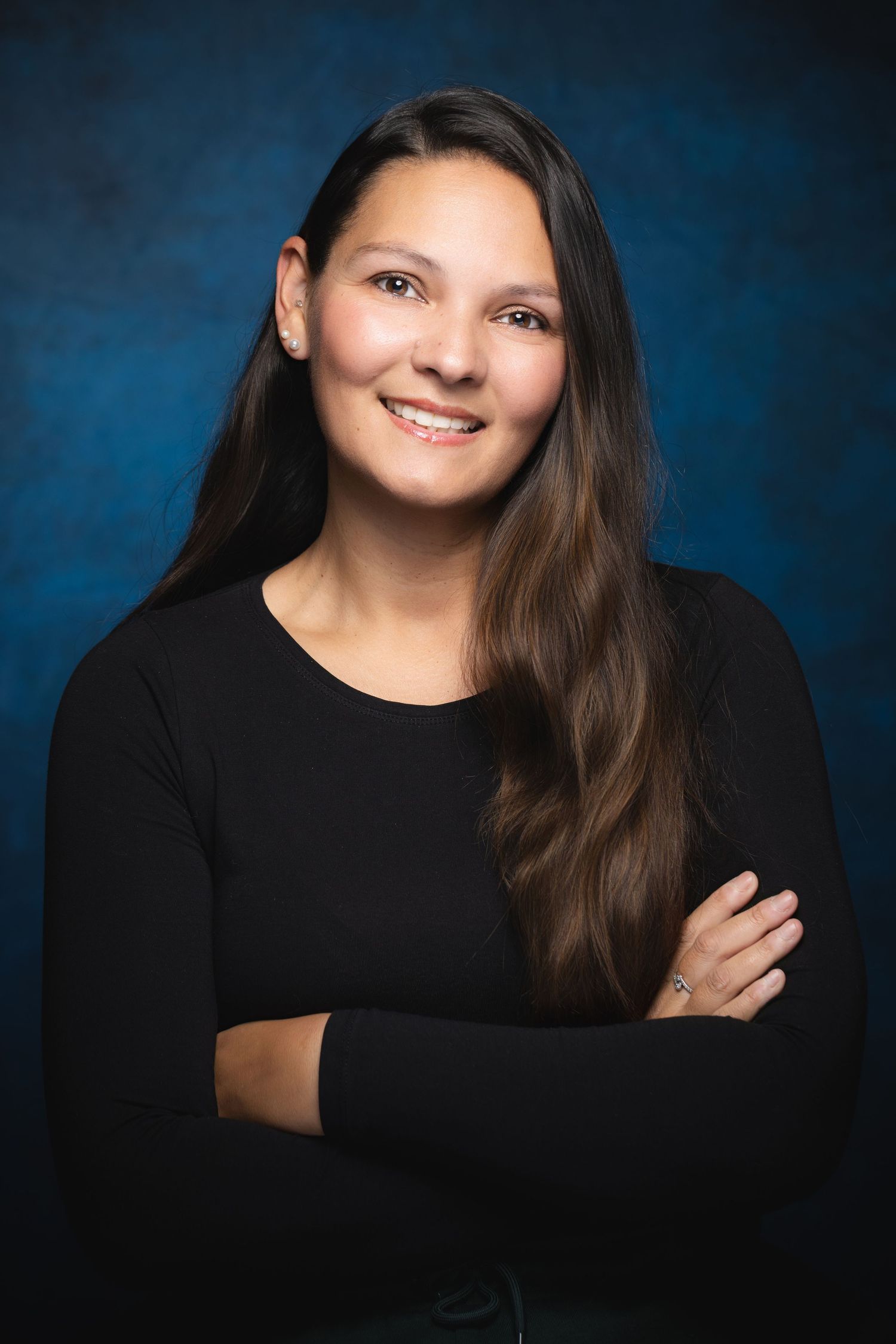 Professional headshot of performer with long dark hair photographed against blue studio backdrop at Castle Theatre Wellingborough