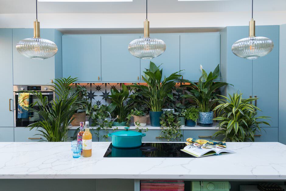 Modern kitchen interior with pendant lights, white countertops, and tropical houseplants adds fresh style to the space.