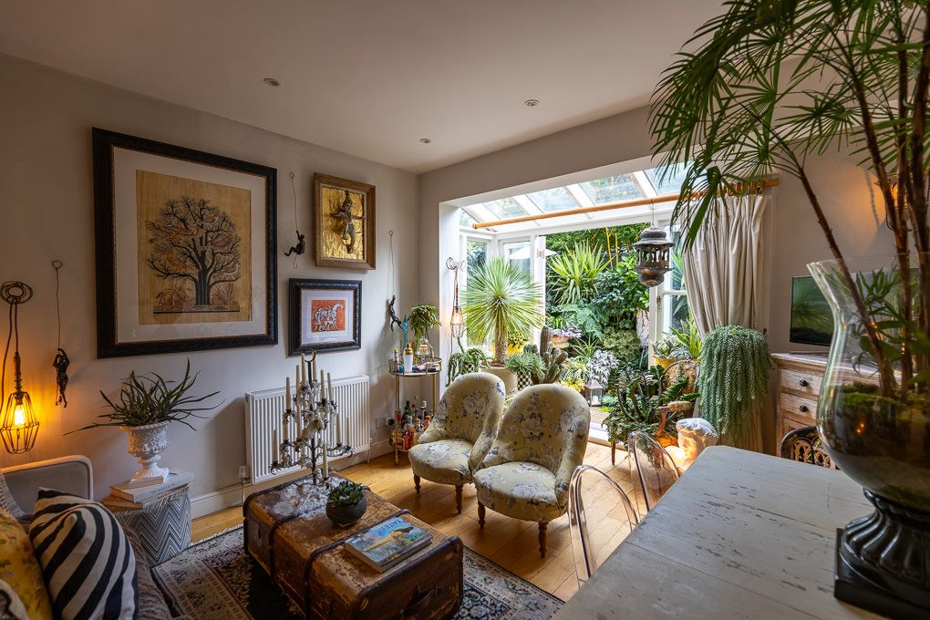 Property photo of a modern coastal-inspired living room features houseplants, neutral decor, and large windows overlooking landscaping.