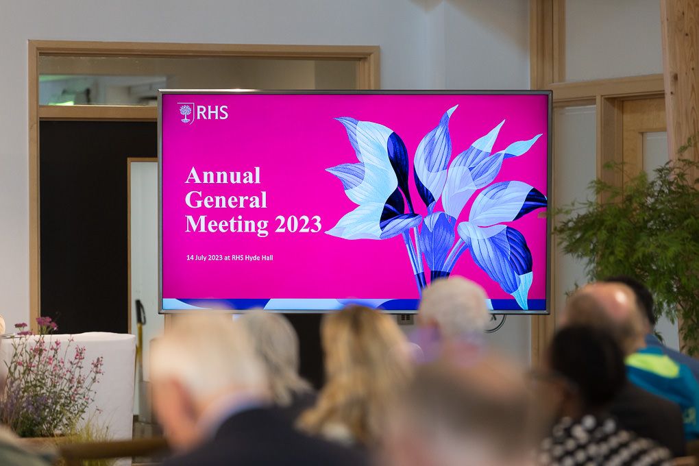 Conference attendees gather in a modern meeting space with bright pink digital displays showing 