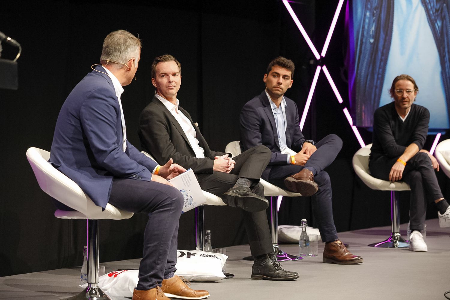 Four business professionals engaged in a panel discussion seated on white chairs at a corporate conference event.