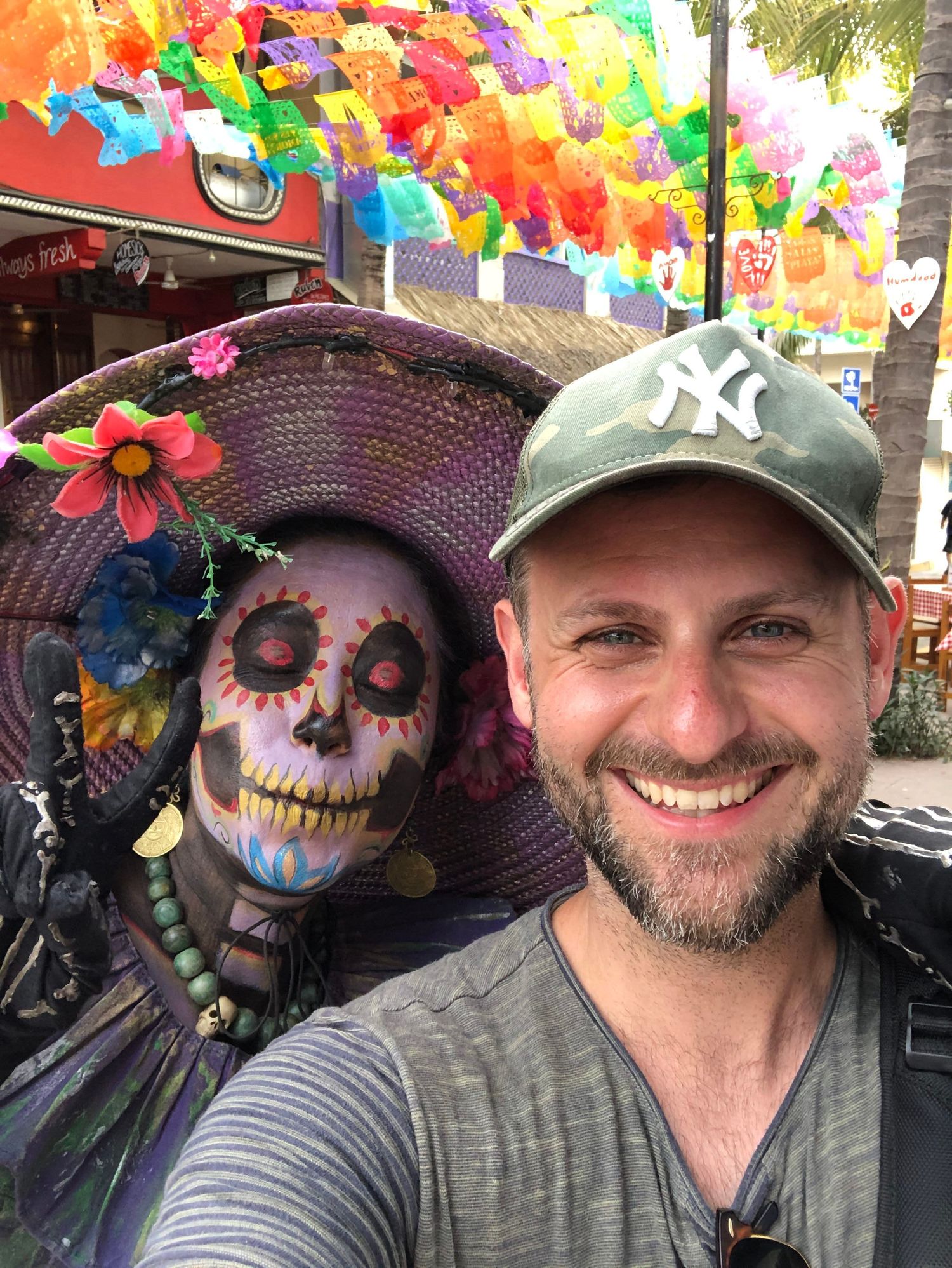 Photographer Lee Charlton smiling next to a colourful Day of the Dead skeleton statue while on assignment in Mexico.