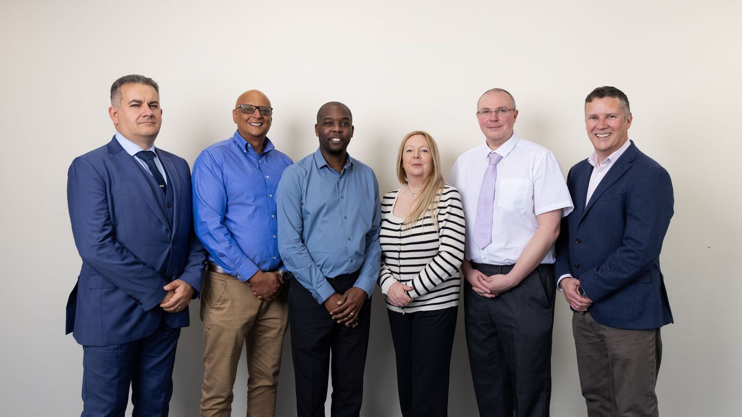 Six business professionals posing together for a group photo against a neutral background.