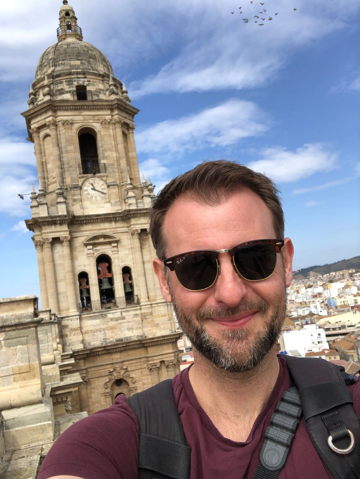 Man in sunglasses taking a selfie in front of a historic church tower under a blue sky.