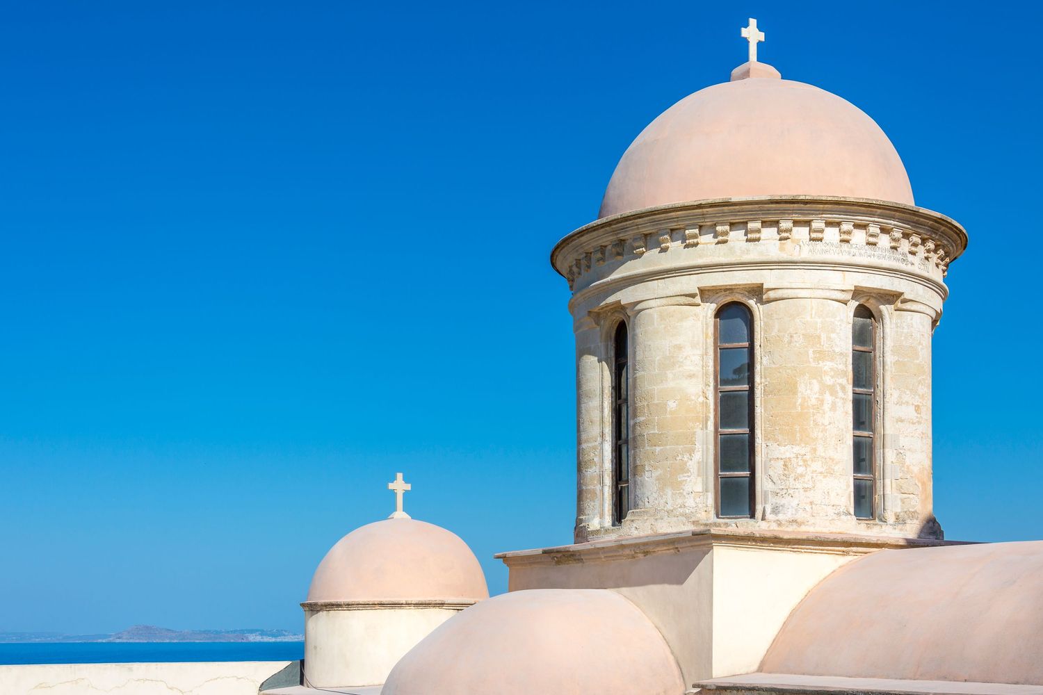 Two pink domed church towers with crosses against a clear blue sky in a Mediterranean setting.