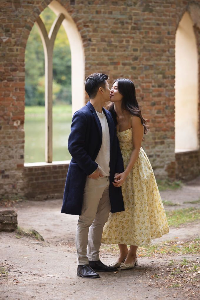 A romantic couple shares tender kisses under a brick archway in Painshill Park, Surrey.