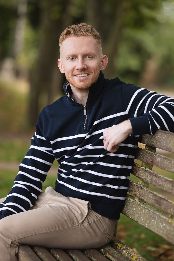 A person wearing a navy striped sweater reclines on a wooden park bench in a natural outdoor setting.