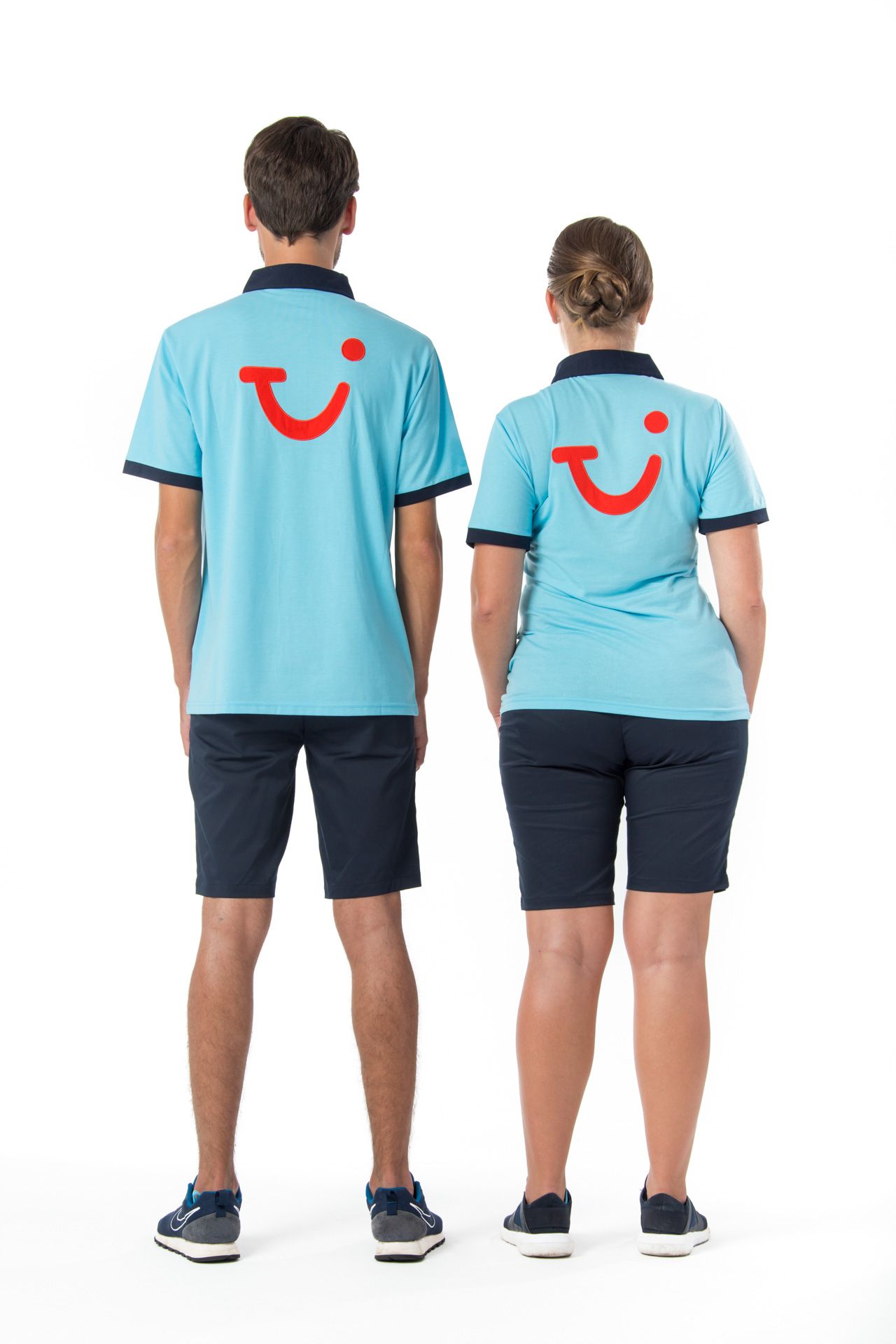 Two employees in light blue TUI uniforms with red smile logos stand back to back wearing navy shorts and boat shoes.