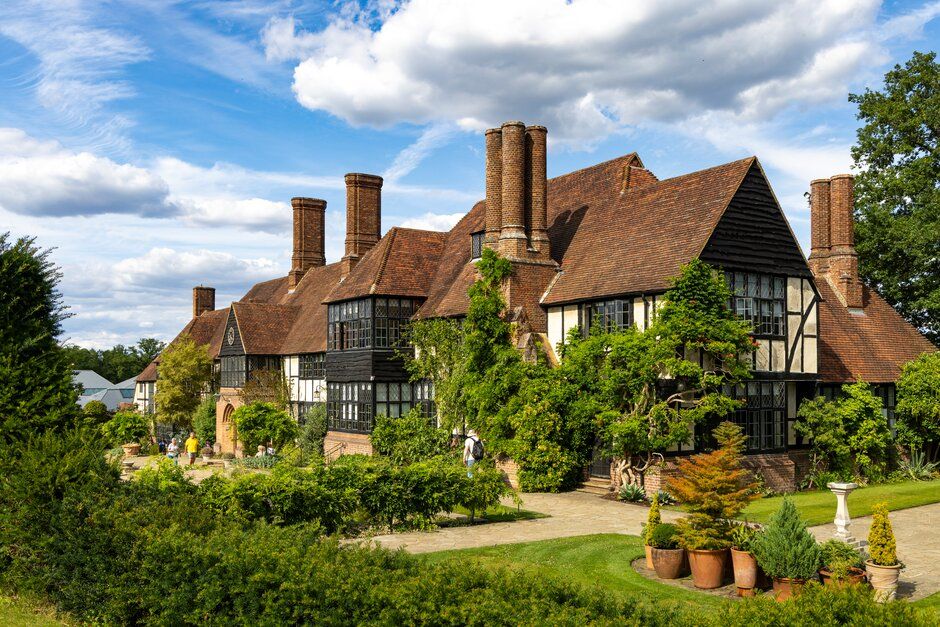 Tudor-style manor house with timber framing and tall brick chimneys surrounded by manicured gardens.