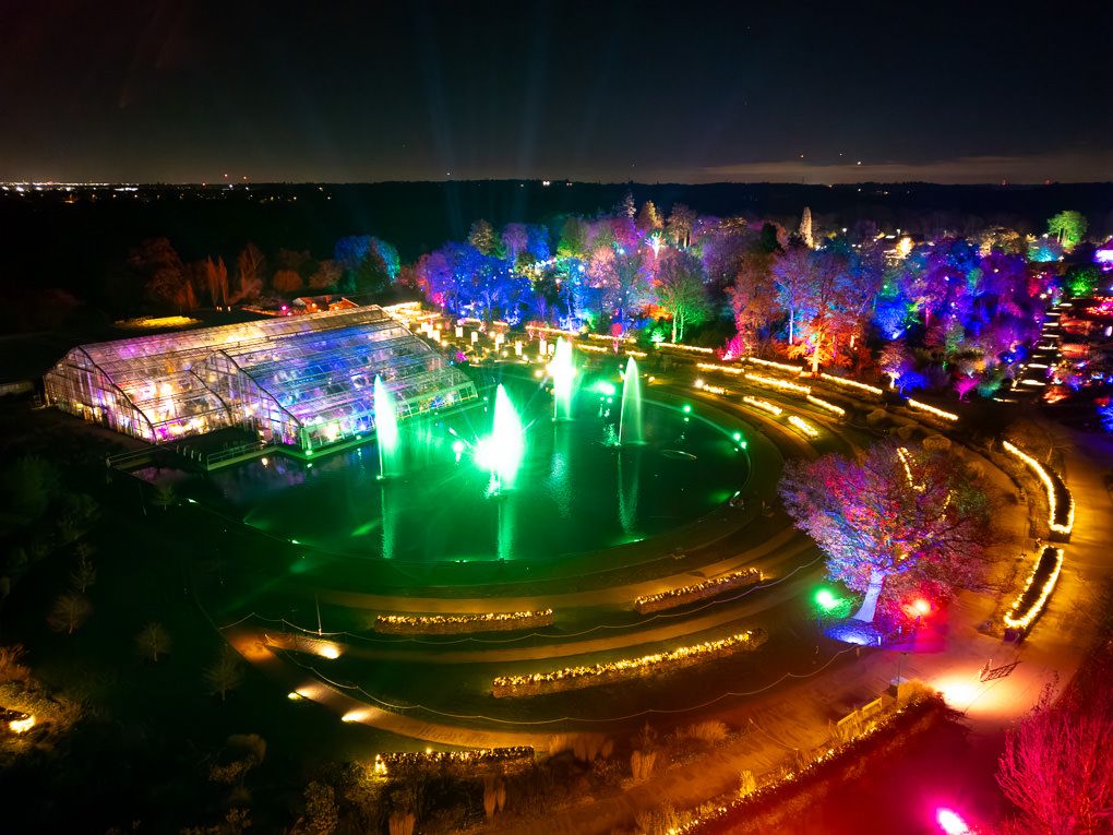 Aerial view of colourful illuminated landscapes with winding paths and vibrant LED lights creating a magical nighttime display at RHS Wisley