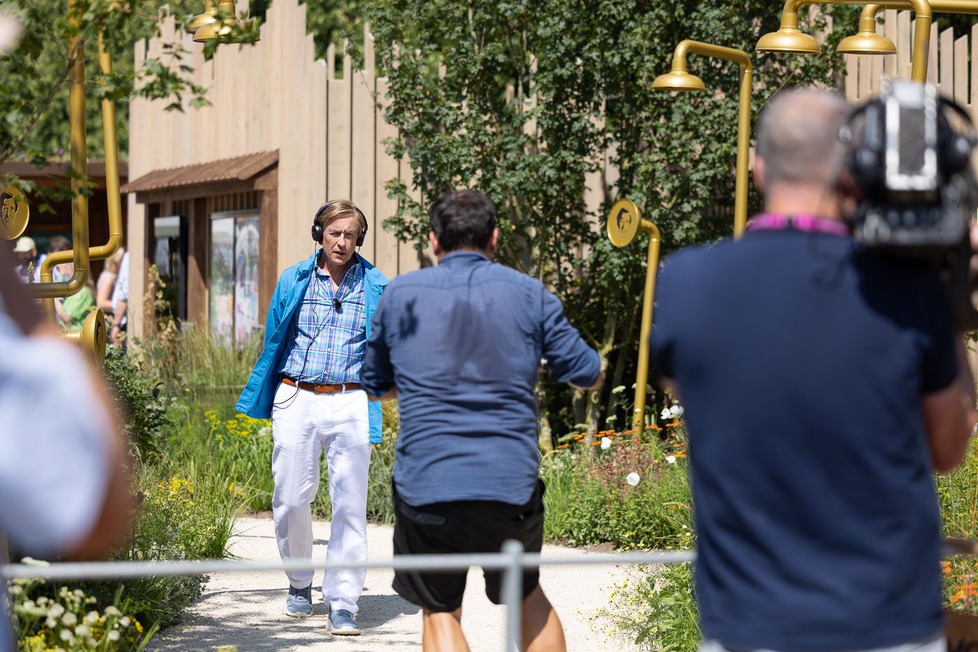 Behind-the-scenes film shoot with Alan Partridge and the Audible film crew on garden pathway in sunny outdoor setting.