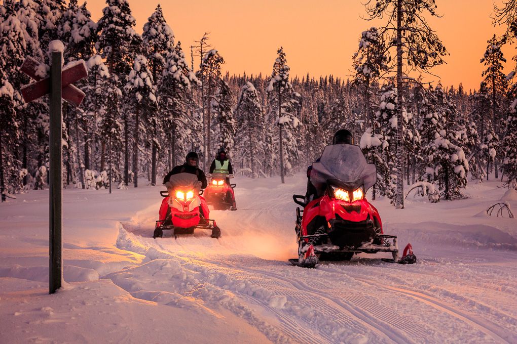 A snowy winter landscape at sunset with snowmobile tracks winding through a snow-covered forest path in Finland. Excursion photography.