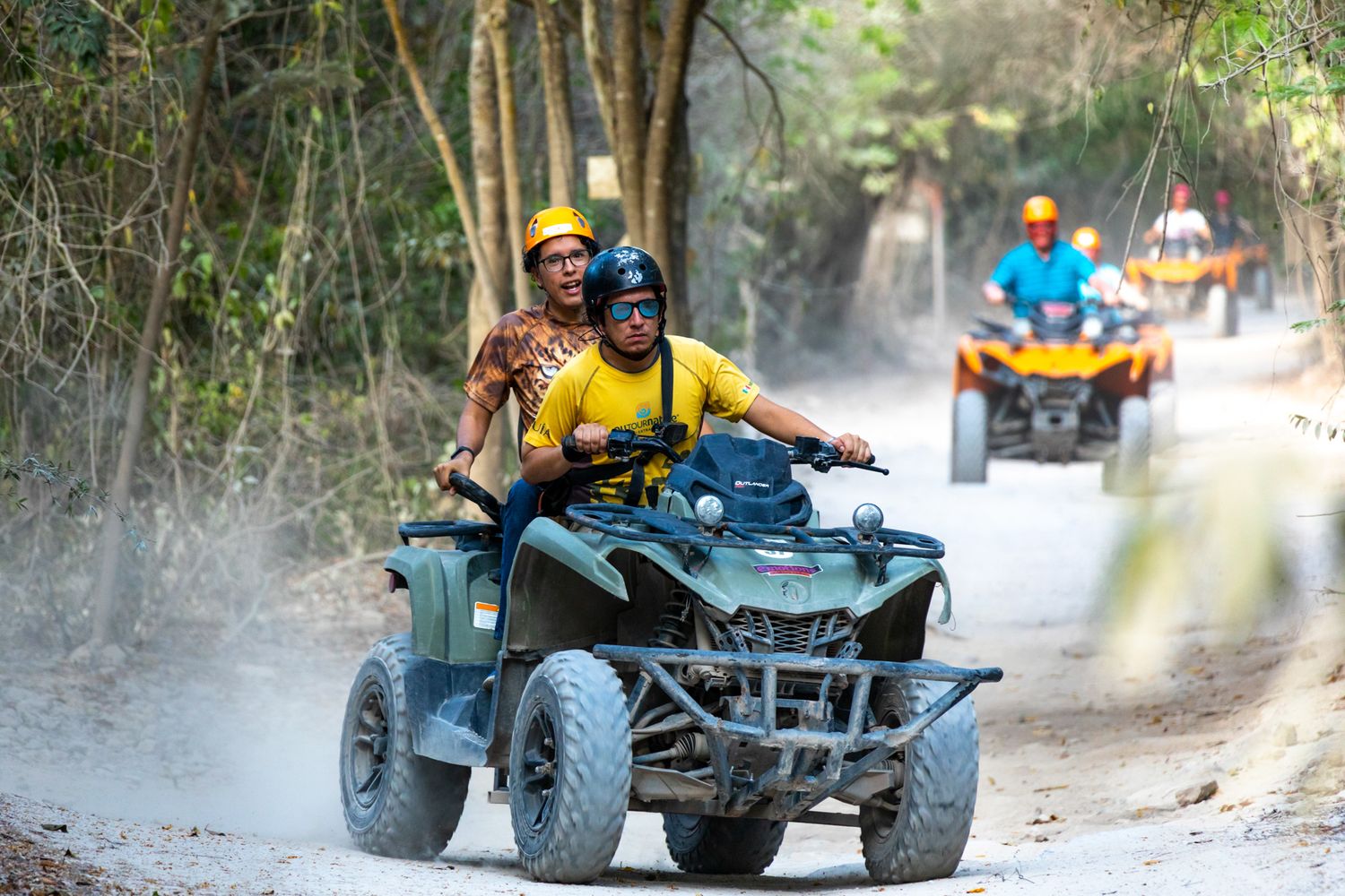 A group of people riding ATVs on a dusty forest trail during an adventure excursion.