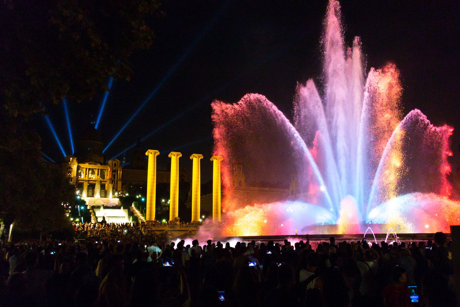 Illuminated water fountain display with colorful lights and historic columns at night in Barcelona's Magic Fountain show.