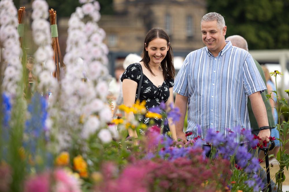 Two people walking together and smiling while admiring colorful summer flowers in a blooming garden.