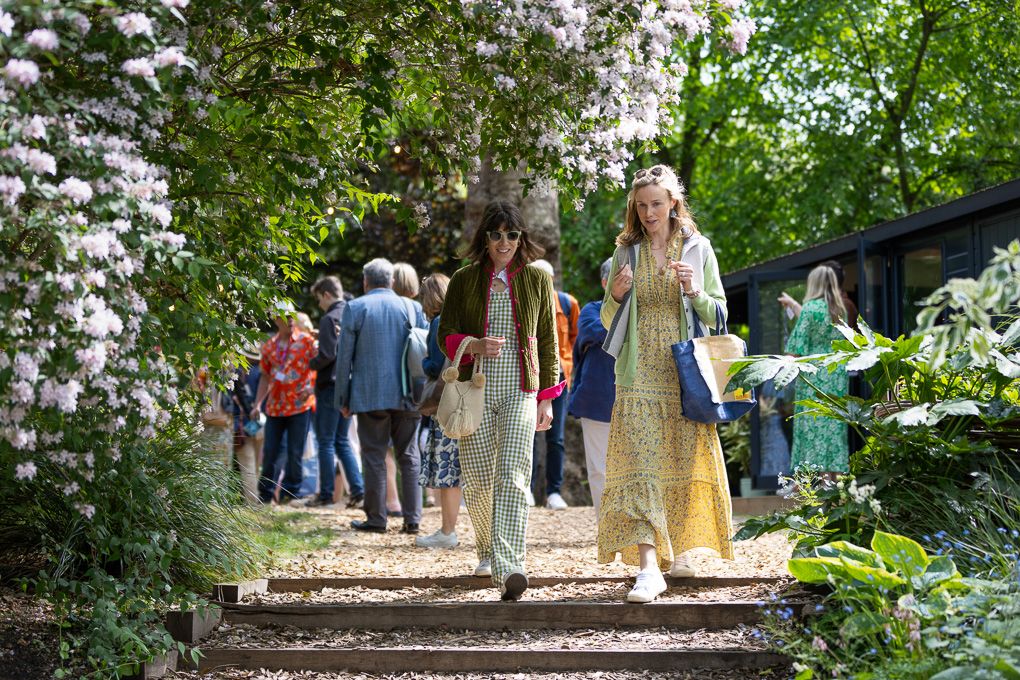 People walking along a garden path at RHS Chelsea Flower Show in London on a sunny day.