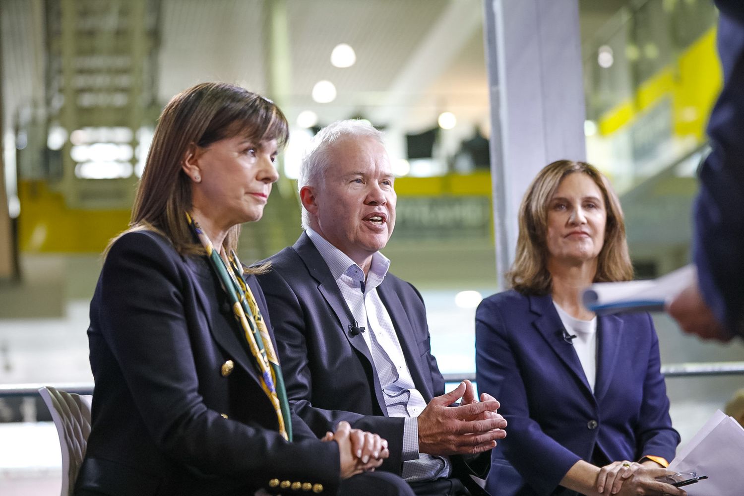Three business professionals seated together at a panel discussion in a modern office setting.