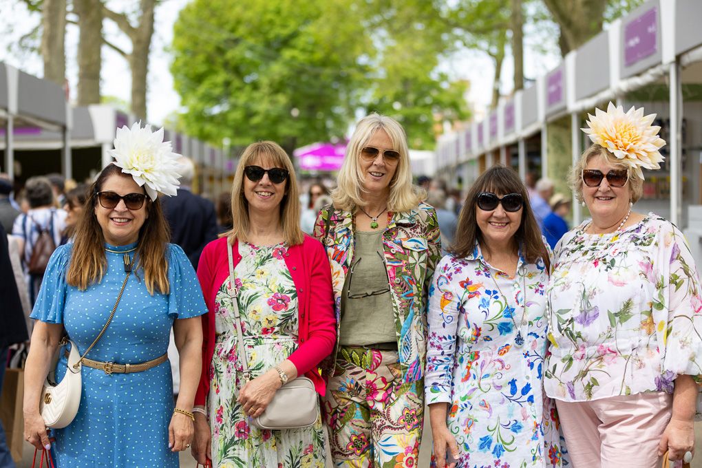 A group of people wearing colorful floral outfits and sunglasses gather in London at the RHS Chelsea Flower Show.