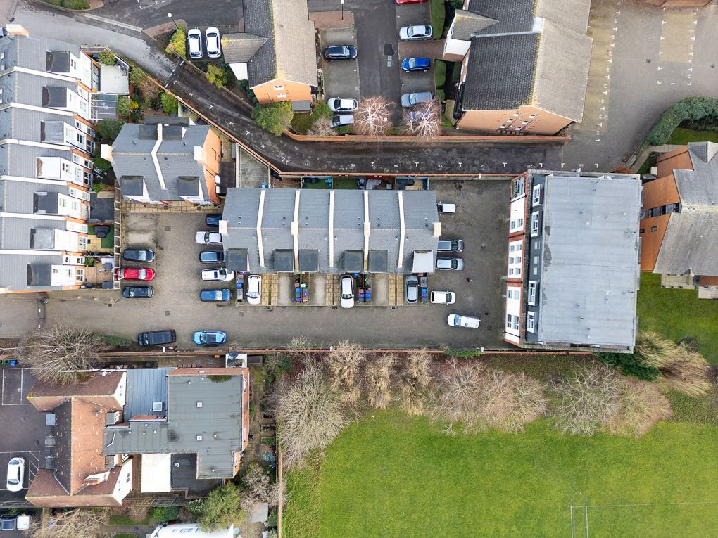 Aerial view of residential neighbourhood showing houses, parked cars, and green spaces from above.