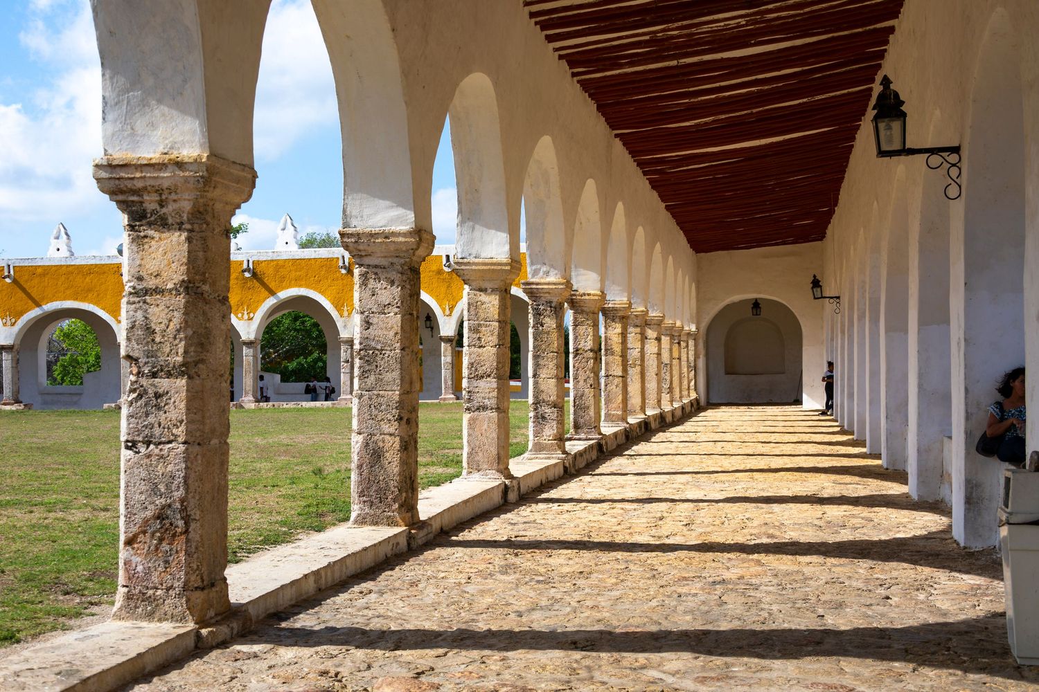 Sunlit colonial arched corridor with stone columns and cobblestone floor at a historic monastery in Izamal, Mexico.