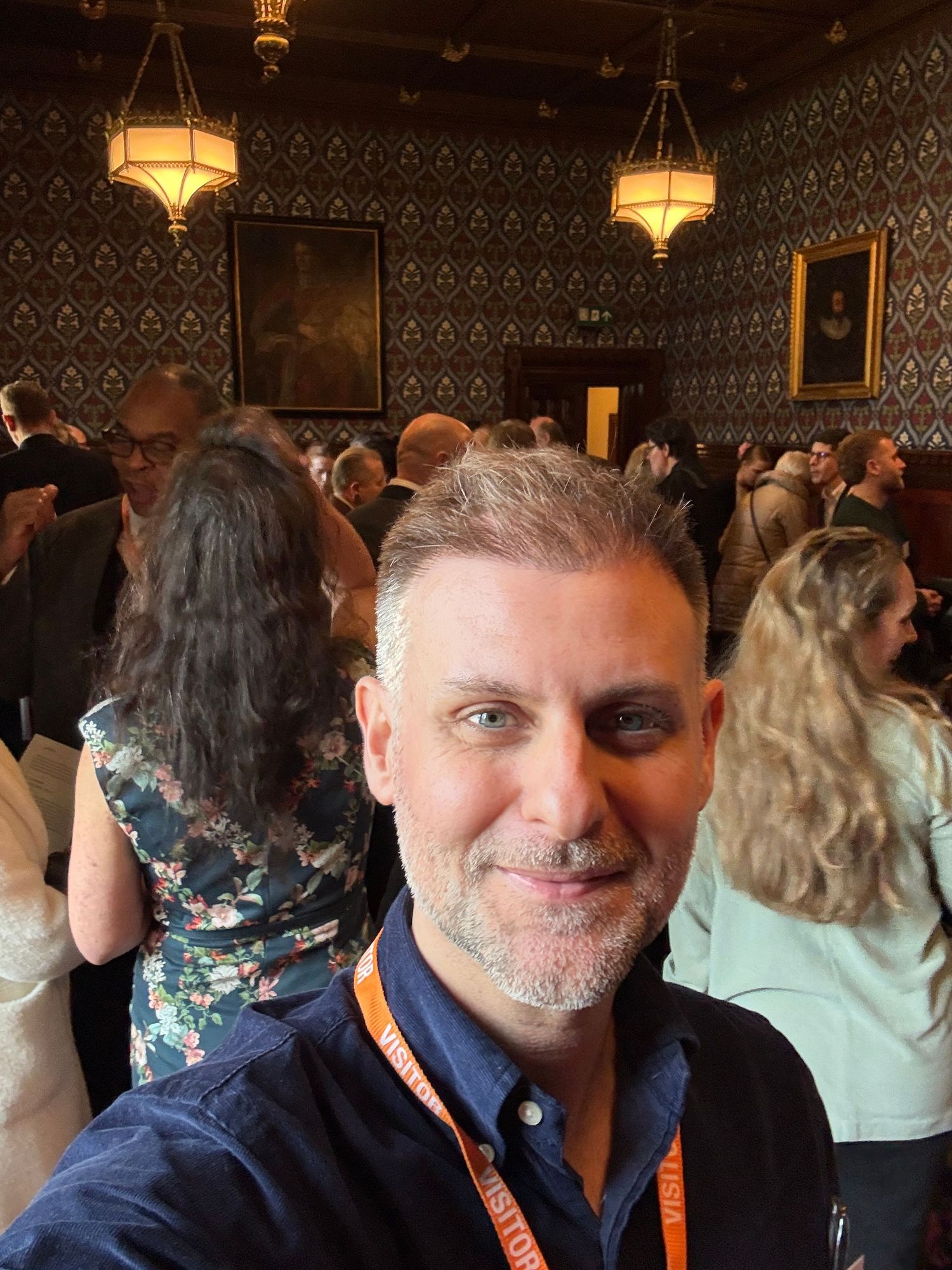 Man taking a selfie at an elegant indoor gathering with ornate wallpaper and warm lighting in a historic venue.