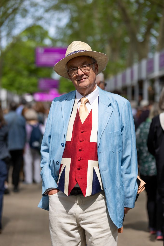 A person wearing a light blue blazer, a Union Jack vest, and a straw hat wandering around the RHS Chelsea Flower Show.