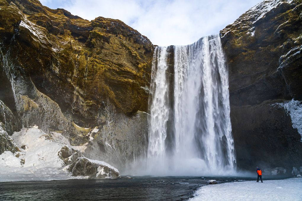 Skógafoss Waterfall cascades down snow-covered cliffs in winter, creating a dramatic natural landscape in Iceland.