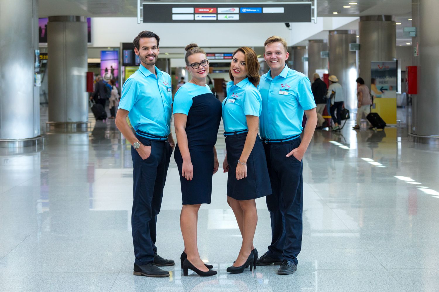 Group of TUI reps in light blue uniforms with red TUI logo pose together in an airport terminal.