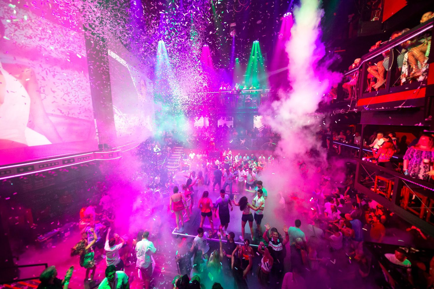 Crowd enjoying a live nightclub event with colourful lighting, smoke effects and confetti.