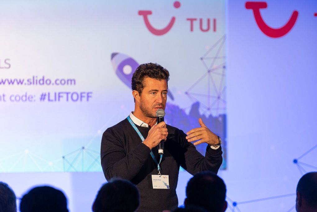 Conference photography of a person in a suit speaking on stage at a TUI business conference event in London.