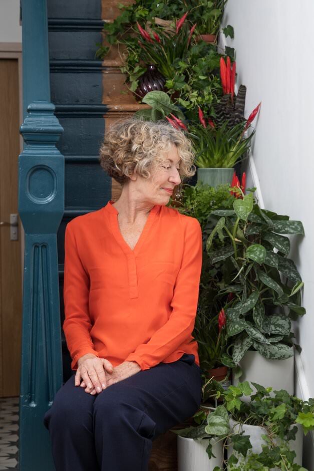 A lifestyle shoot of a lady sitting on steps near a decorative blue railing and potted plants with red flowers.