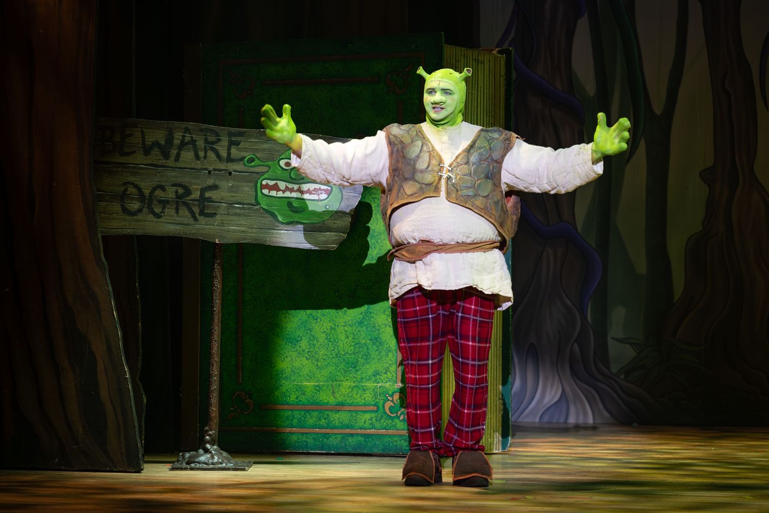 Actor as Shrek in green costume with ogre ears performs beside a “Beware Ogre” sign during Shrek The Musical in Wellingborough