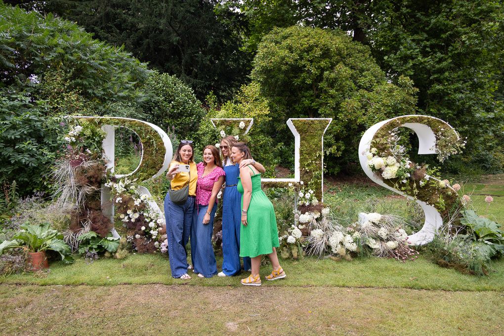 People gathered in front of a decorative botanical garden wall with large stone letters spelling out DUKE.