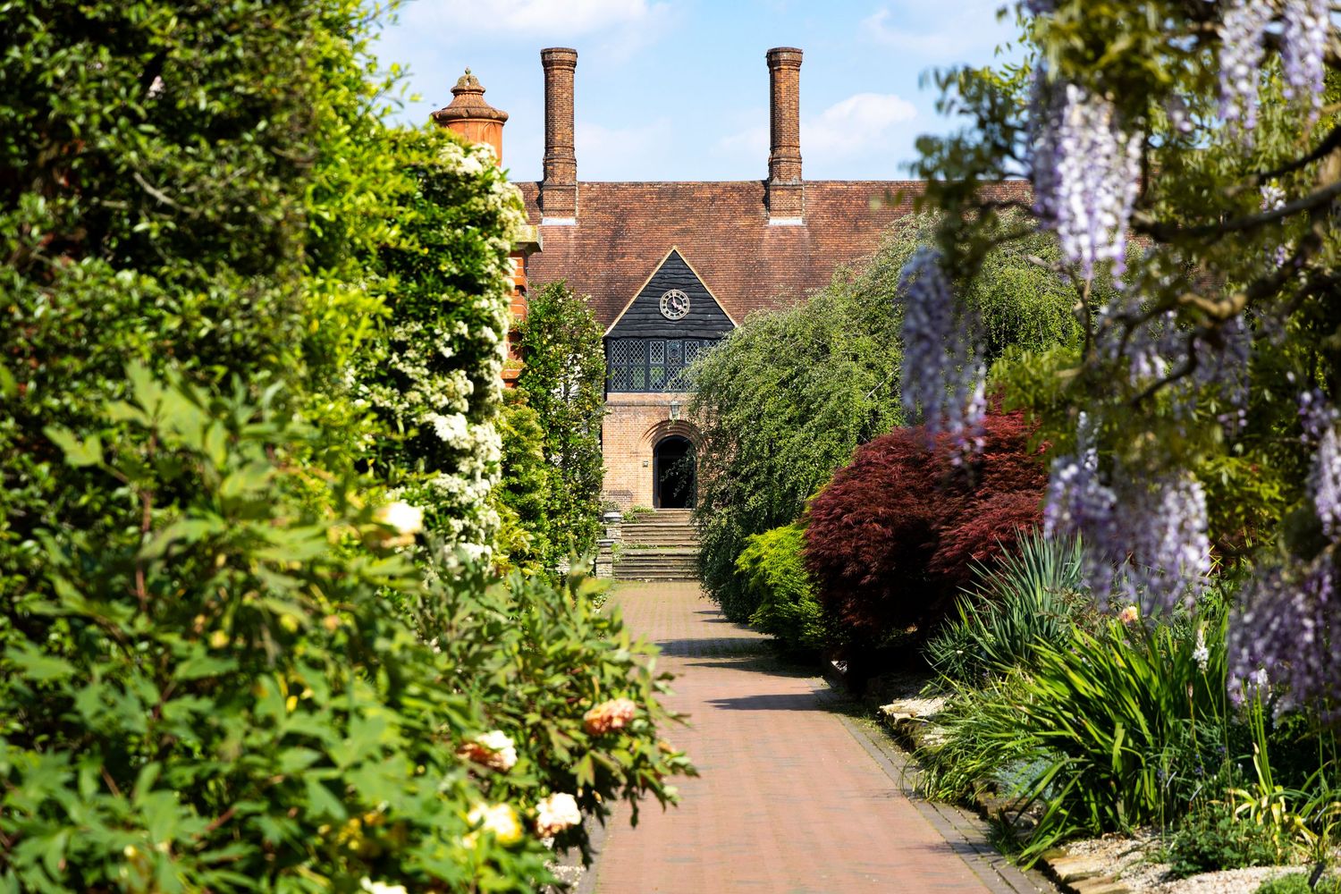 Historic manor house approached via landscaped gardens and flowering borders showcasing luxury estate grounds.