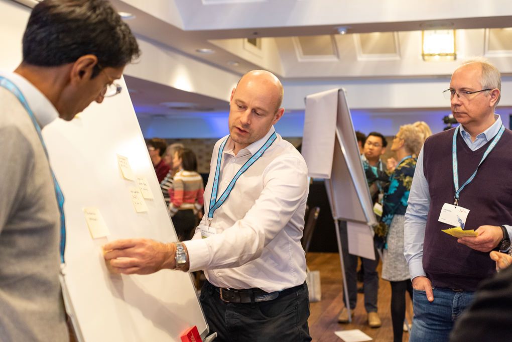 Business professionals gather at a conference event in London. They are interacting and exchanging information on a whiteboard.