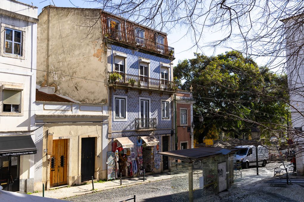 Old European street view with rustic buildings, balconies, and a green tree in a quiet residential neighborhood.