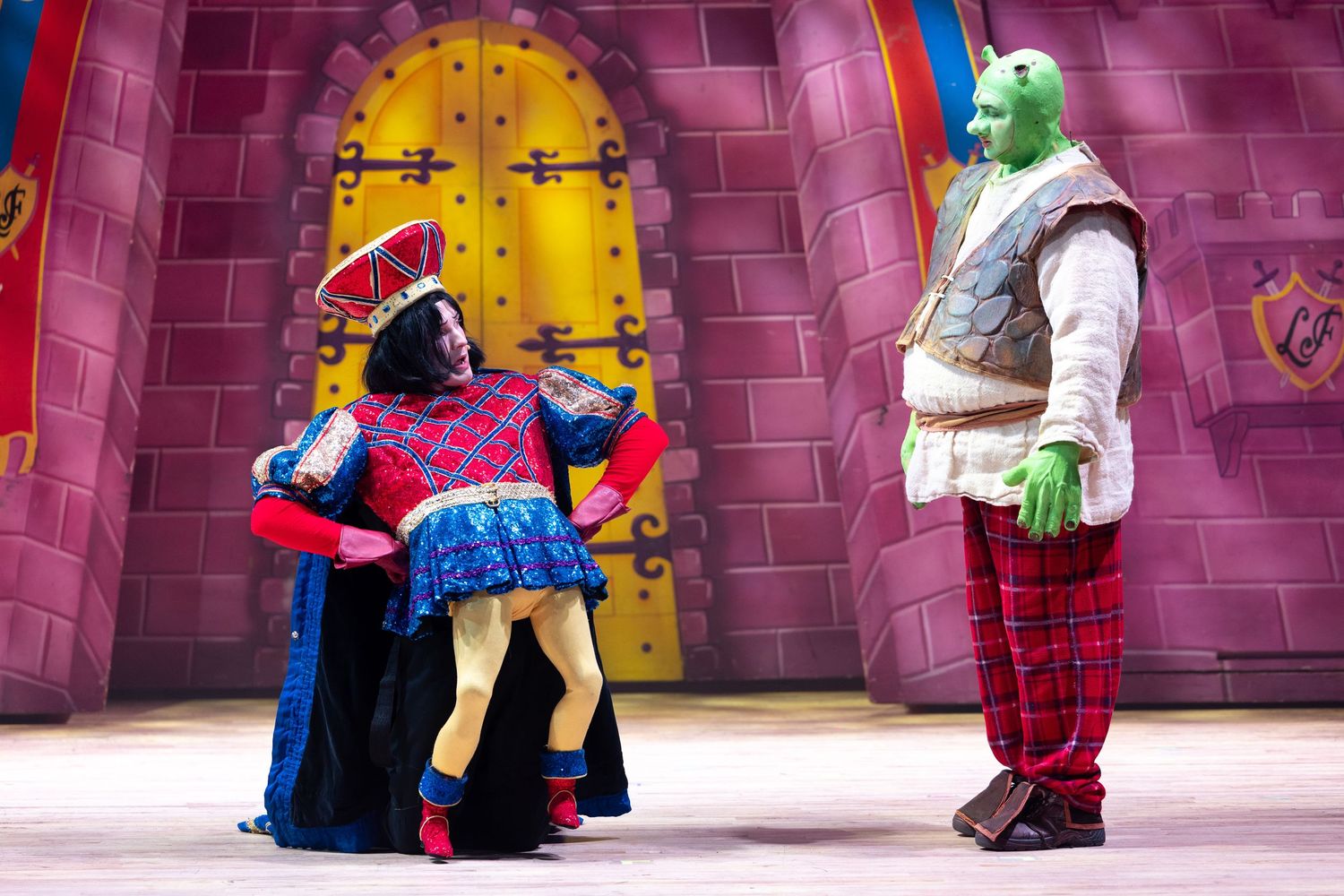 Shrek and Lord Farquaad perform on stage in colourful costumes during Shrek The Musical at Castle Theatre, Wellingborough