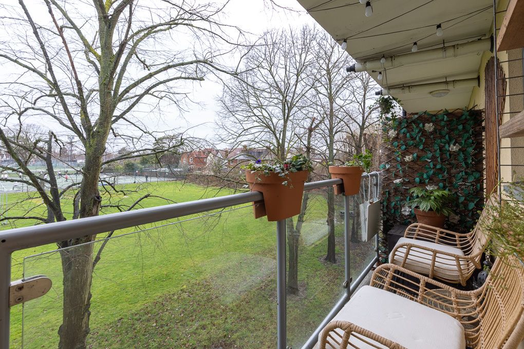 Property photography of cosy rattan chairs with plush cushions on a balcony overlooking scenic fields and trees.